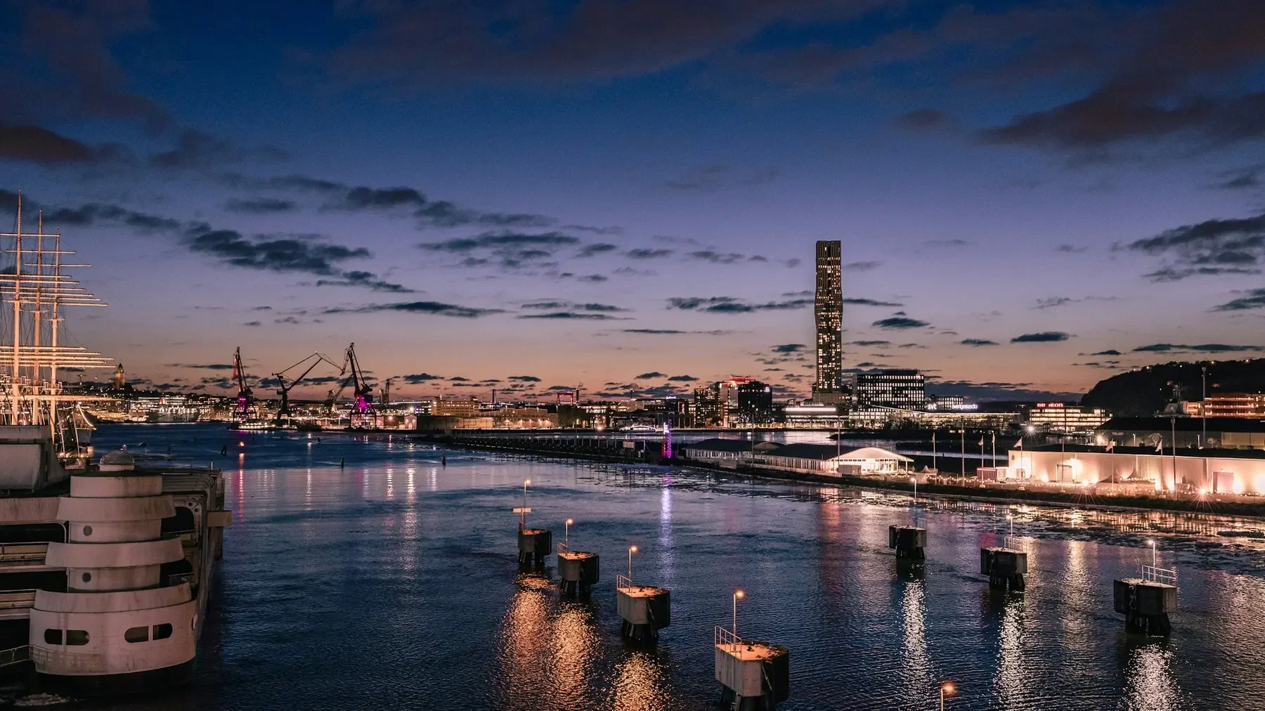 Göteborgs hamn i skymning, med stadens ljus som speglas i älven och ett höghus i fjärran.