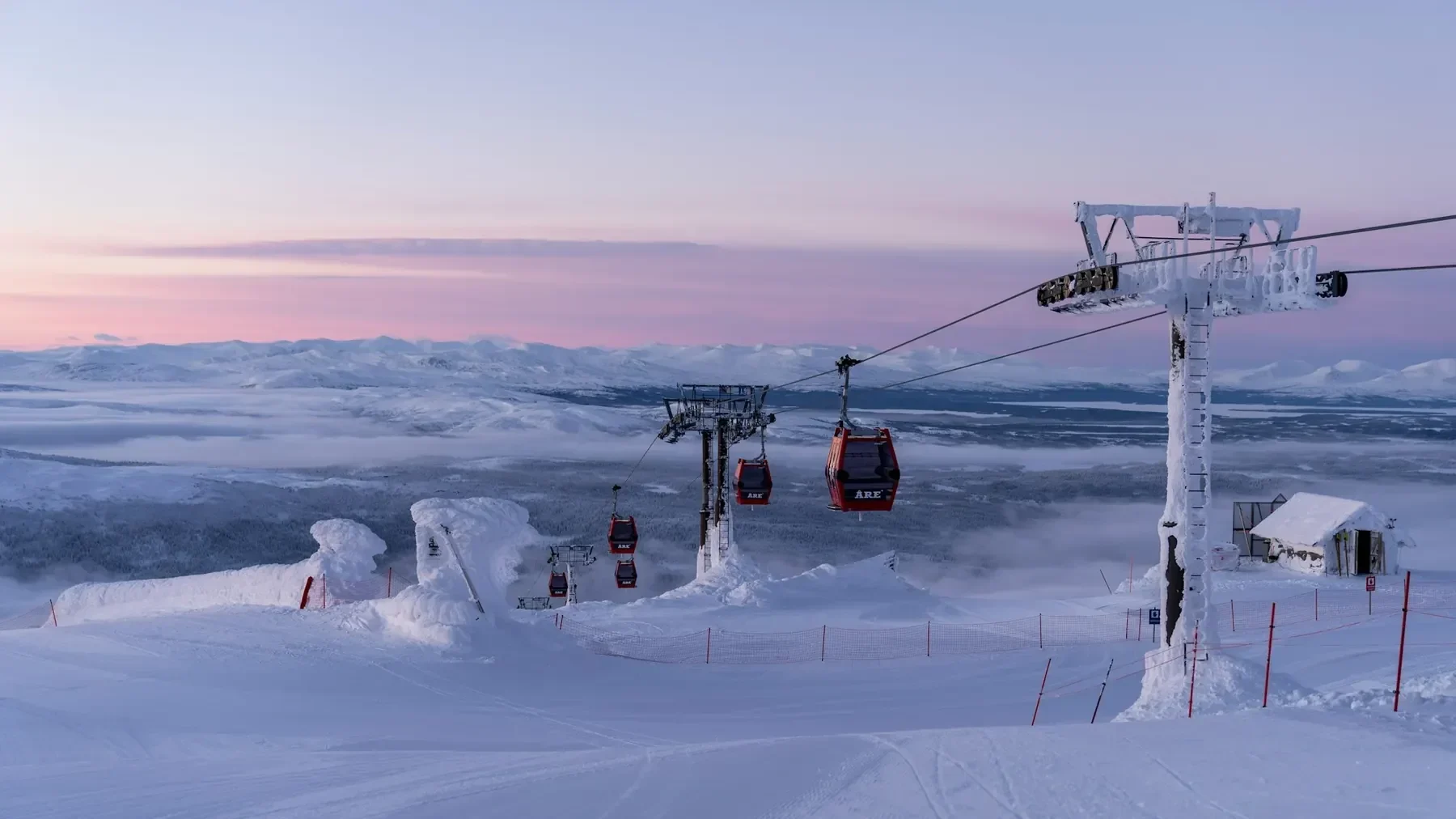 Snötäckt fjälltopp i gryningsljus med en gondollift och frostiga liftstolpar.