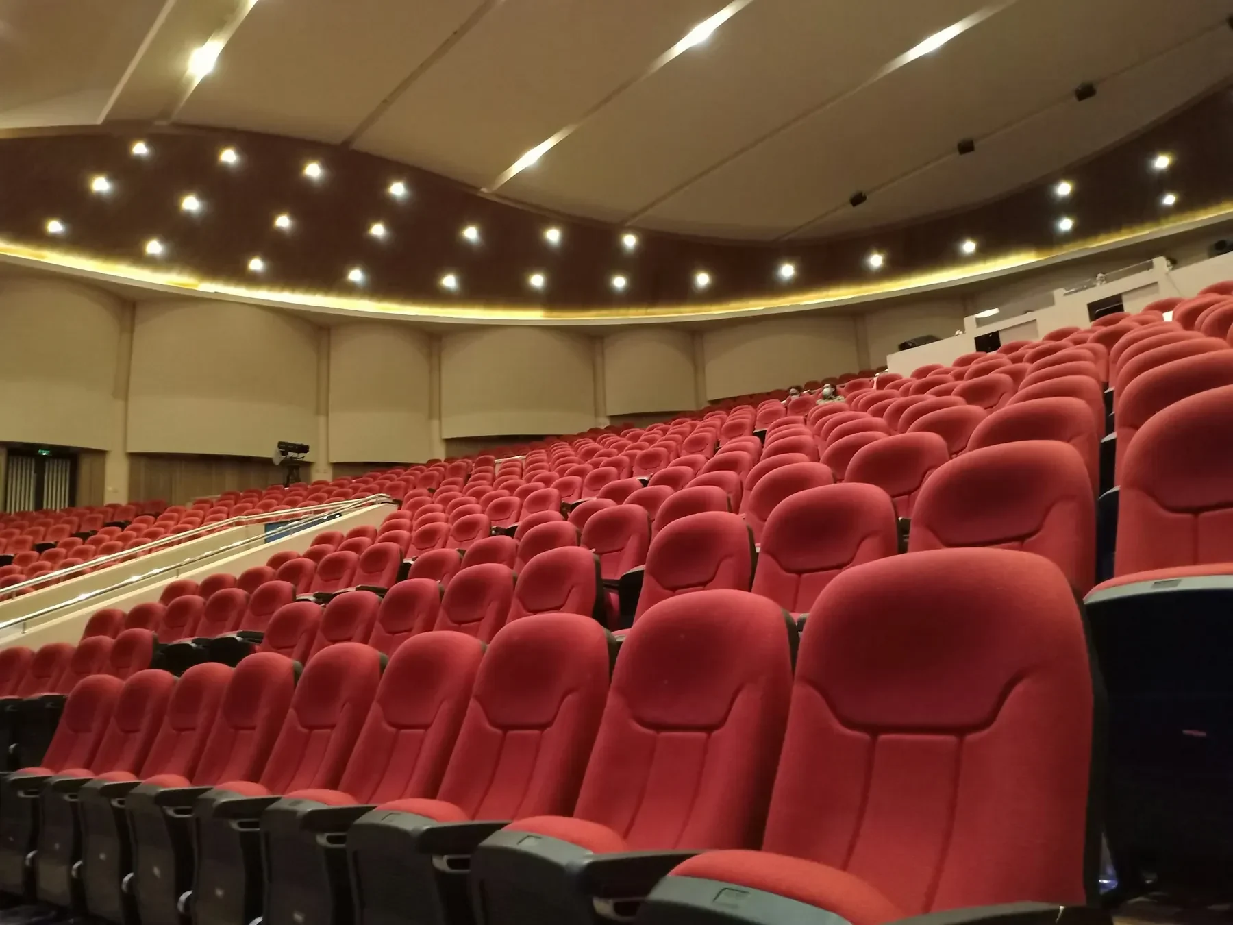 Stort tomt auditorium med rader av röda stolar under ett tak med spotlights.